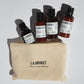 Set of L:A Bruket skincare products in a beige pouch on a light gray background